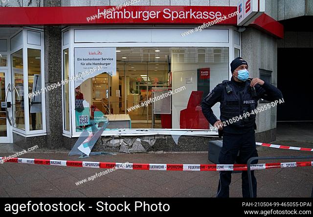 04 May 2021, Hamburg: A policeman stands in front of the window of a Haspa branch that was destroyed in an accident. In Waitzstraße in Hamburg