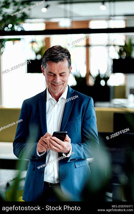 Smiling businessman using smart phone standing at office