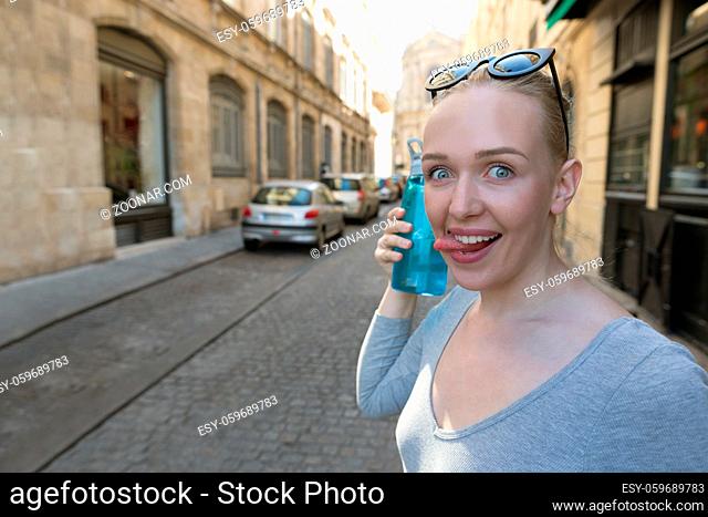 Portrait of a woman fooling around with a bootle of water. She is playing with her tongue
