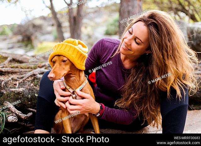 Smiling woman sitting with dog in forest at La Pedriza, Madrid, Spain