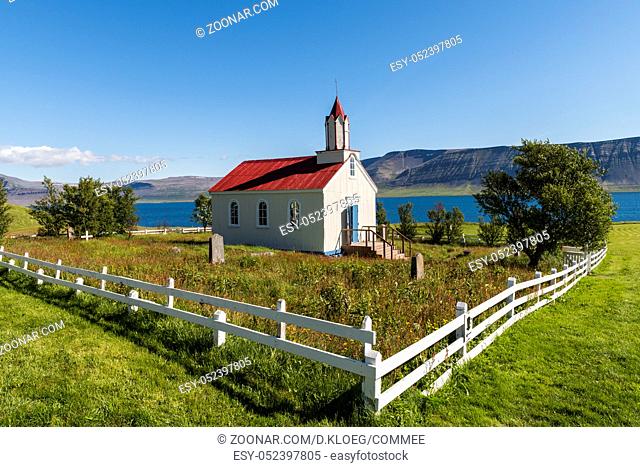 Wooden church with red roof and white fence at Hrafnseyri on Iceland on a summers day with blue sky