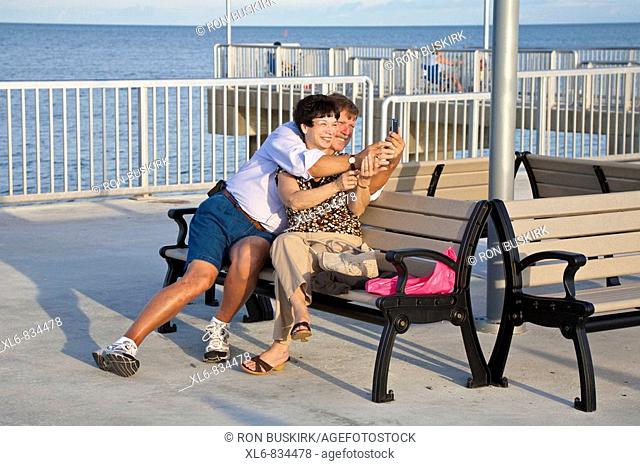 Man and woman couple take photos while sitting on bench on fishing pier at Cedar Key, Florida