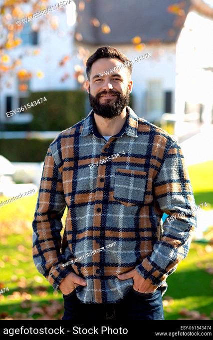Portrait of happy caucasian man with beard standing and smiling to camera in sunny autumn garden