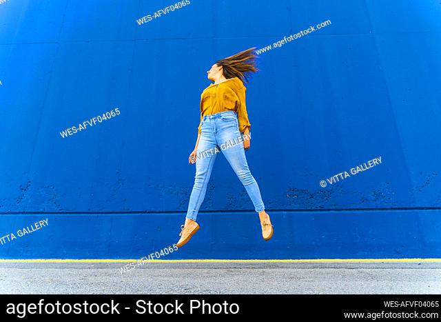Young woman jumping in front of a blue wall