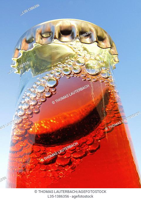 Shaken bottle neck with crown cap and a red liquid and many bubbles