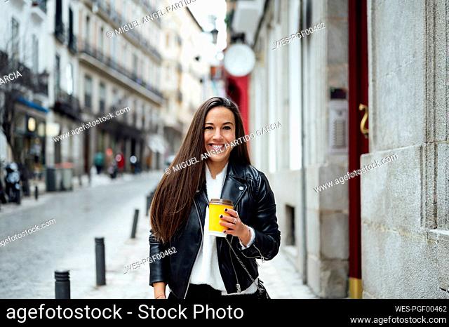 Mid adult woman holding reusable cup while standing at street in city