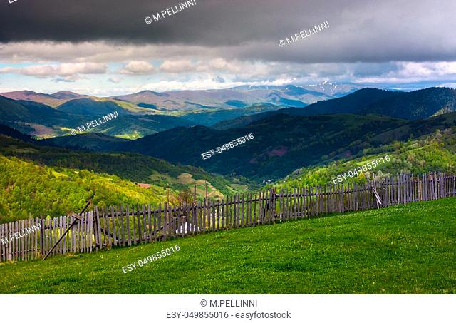 fence on the edge of the hillside. beautiful rural landscape of Carpathian mountains in springtime. forested hills under the heavy clouds in the distance