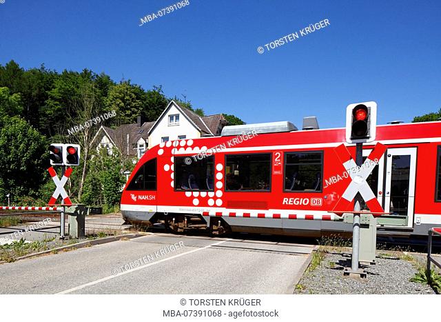 Passing red local train, restricted railroad crossing with closed gate in the Hindenburgallee, Bad Malente-Gremsmühlen, Malente, Schleswig-Holstein, Germany