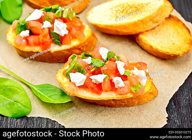 Bruschetta with tomato, spinach and soft cheese on parchment on wooden board background