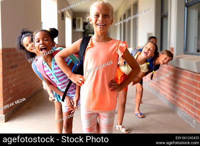 Portrait of smiling playful multiracial elementary school students standing in row at school