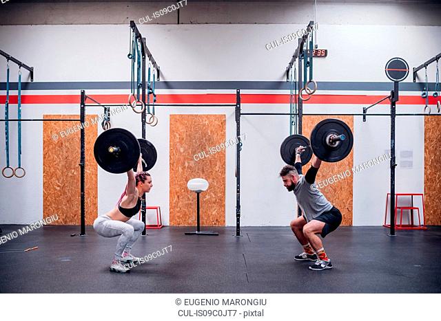 Young couple squatting and lifting barbell in gym