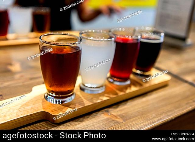 Flight of craft four of different beers glasses, brown black white and red beer on a wooden tray during a tasting session, selective focus, copy space