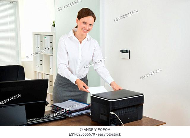 Young Female Secretary Inserting Paper In Printer At Desk