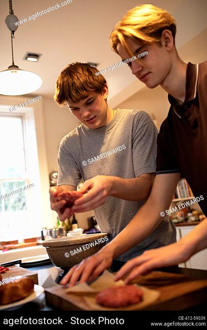 Teenage boys making hamburger patties in kitchen