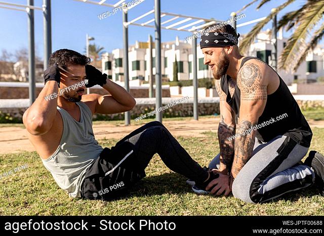 Man helping male friend while practicing sit-ups in park