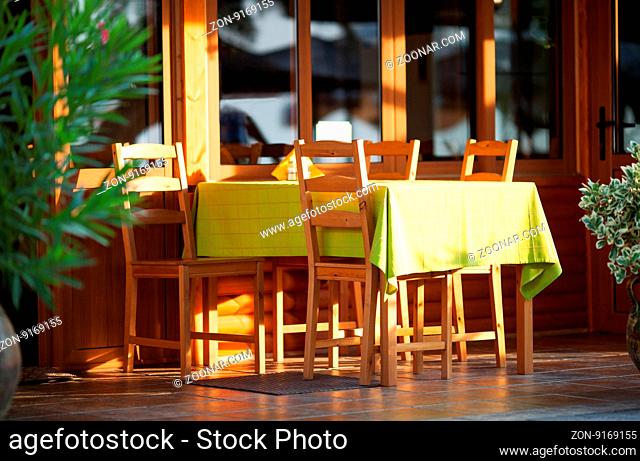 Colorful outdoor table at an open-air restaurant laid with a yellow tablecloth and wooden chairs