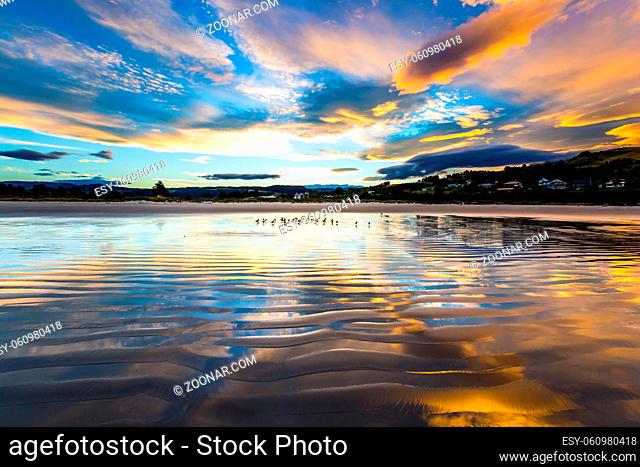 Gentle fancy clouds colors are reflected in the ocean water. Sunset over the ocean. The art of artistic photography. New Zealand, Pacific Coast