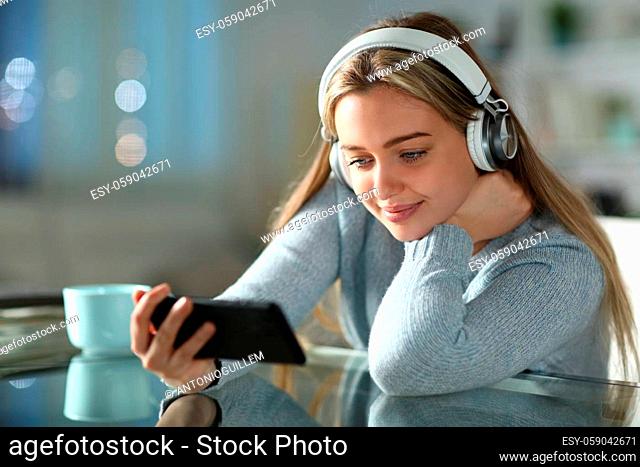 Teen watching videos on smart phone wearing headphones in the night in the living room at home