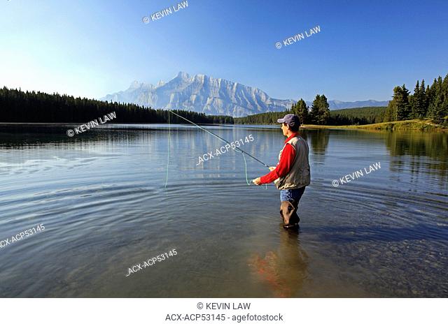 Middle age male fly fishing in mountain lake. Two Jack Lake with Rundle Mountain background, Banff National Park, Alberta, Canada