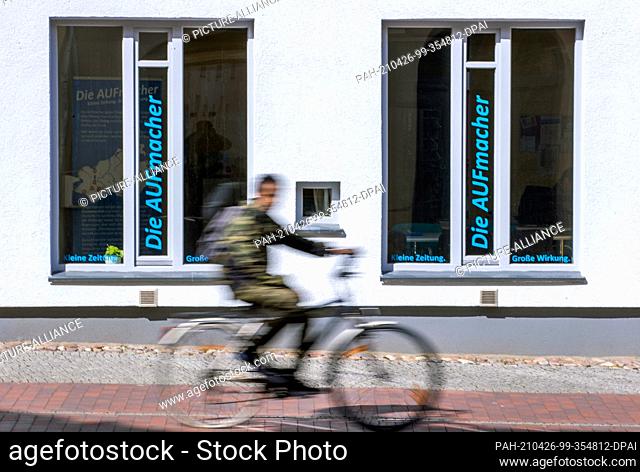 13 April 2021, Mecklenburg-Western Pomerania, Wismar: A cyclist rides past a storefront of a local newspaper with the window lettering ""Die AUFmacher""