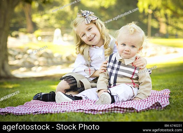 Sweet little girl hugs her baby brother on a picnic blanket outdoors at the park