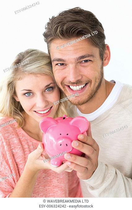 Portrait of attractive young couple holding piggybank over white background