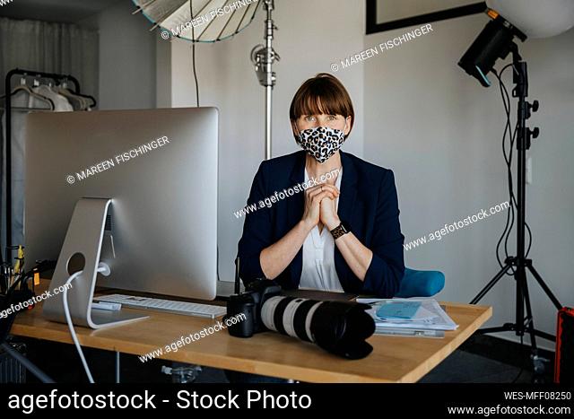 Female photographer with hands clasped sitting in studio during COVID-19