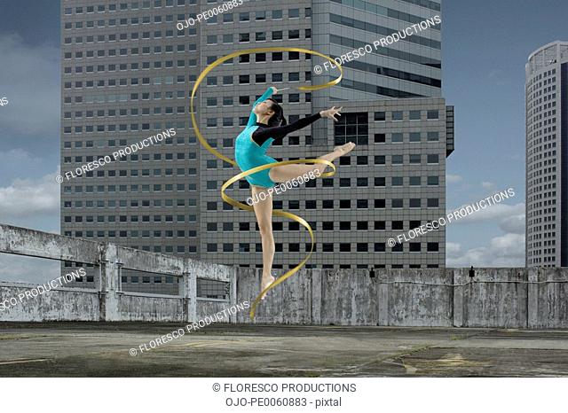 Woman gymnast outdoors on rooftop jumping in air with ribbon