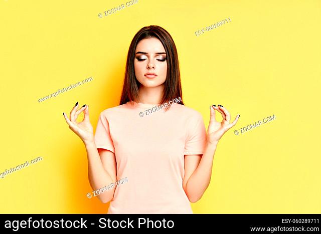 Relaxed pretty woman keeps hands in mudra gesture with eyes closed on yellow background. meditation, patience concept