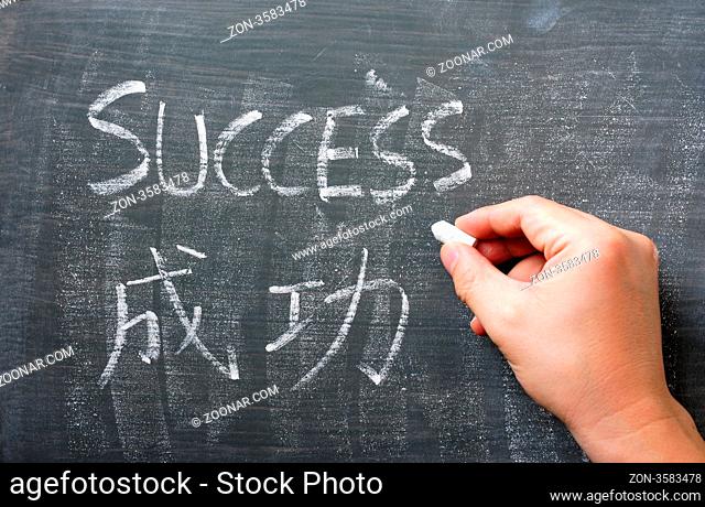 Success - word written with chalk on a blackboard with a Chinese translation, with a hand holding chalk