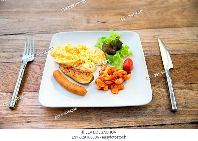 food, dinner and eating concept - scrambled eggs, sausage, chili beans and salad on plate