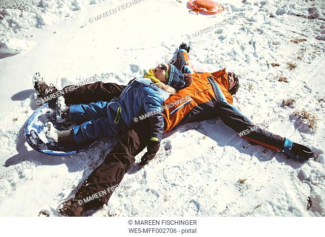 Italy, Val Venosta, Slingia, happy father and son lying in snow