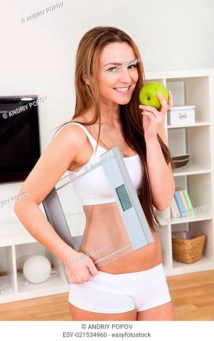 Portrait Of Beautiful Young Woman Holding A Weighing Scale And An Apple