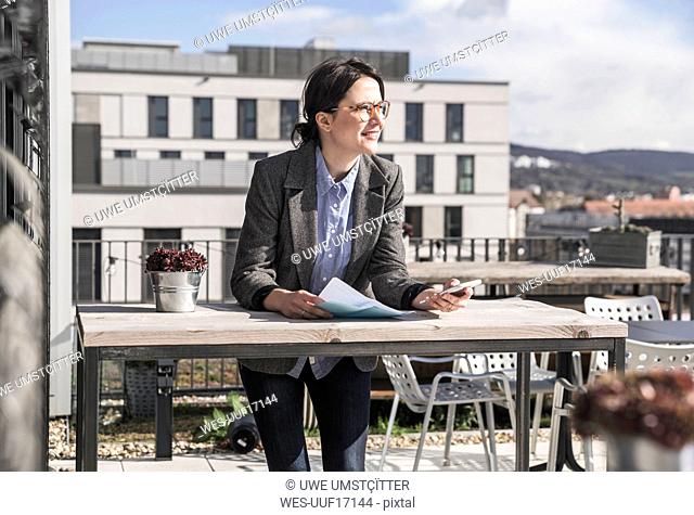 Smiling businesswoman using cell phone on roof terrace