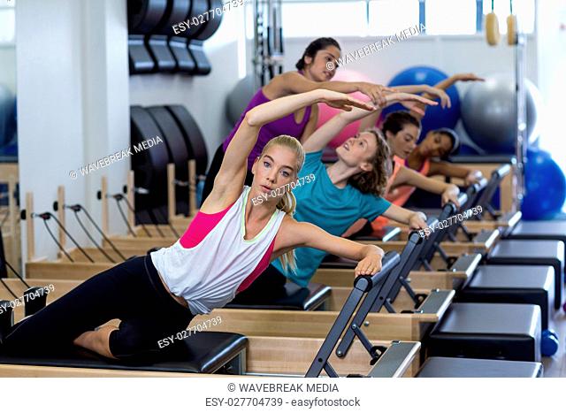 Female trainer assisting group of women with stretching exercise on reformer
