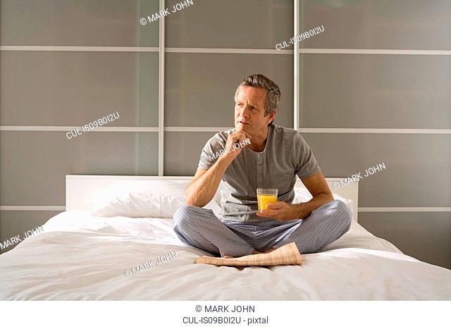 Puzzled senior man sitting cross legged on bed with hand on chin