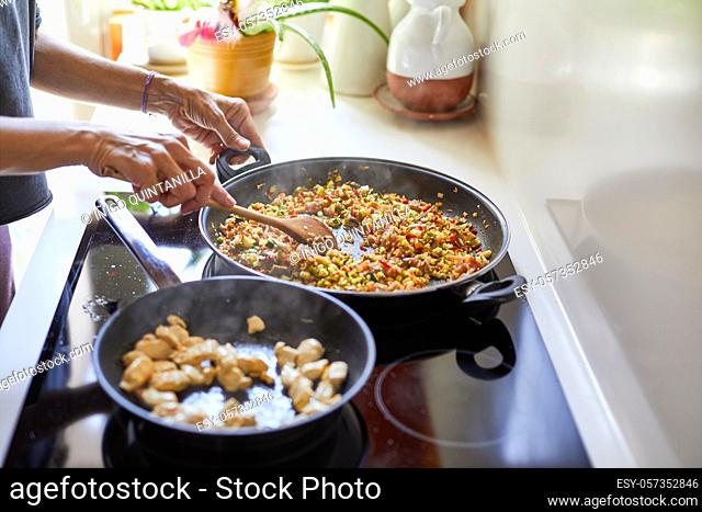 Woman cooking typical Spanish paella with vegetables, rice and chicken in her home kitchen