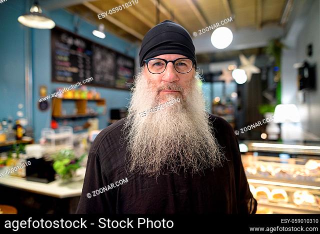 Portrait of mature bearded hipster man with eyeglasses relaxing at the coffee shop indoors