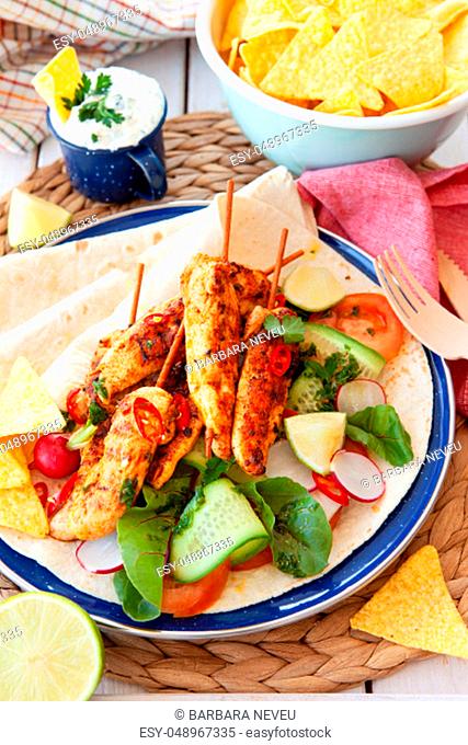 Spicy grilled chicken skewers with fresh salad on tortillas