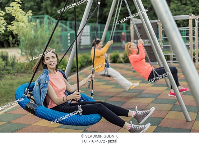 Full length of happy women swinging on swing at playground