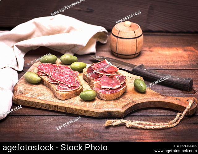 sandwiches with smoked sausage salami and jamon on a wooden kitchen board