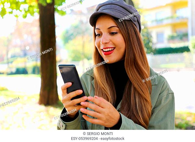 Surprised casual girl wearing hat and polo neck reading good news on smart phone outdoor