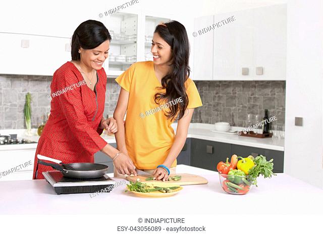 Mother teaching daughter to cut vegetables