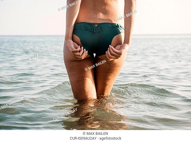 Rear view of young woman adujusting bikini bottoms in sea
