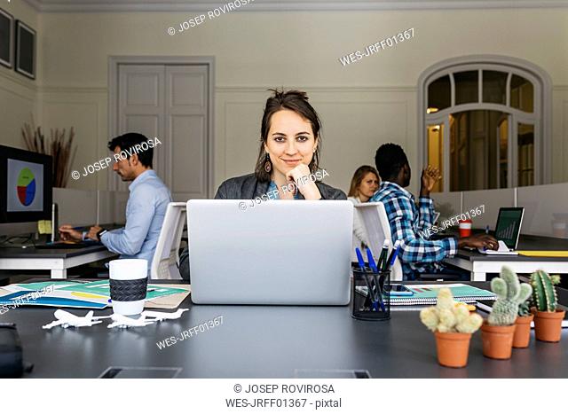 Young businesswoman using laptop, colleagues working in background