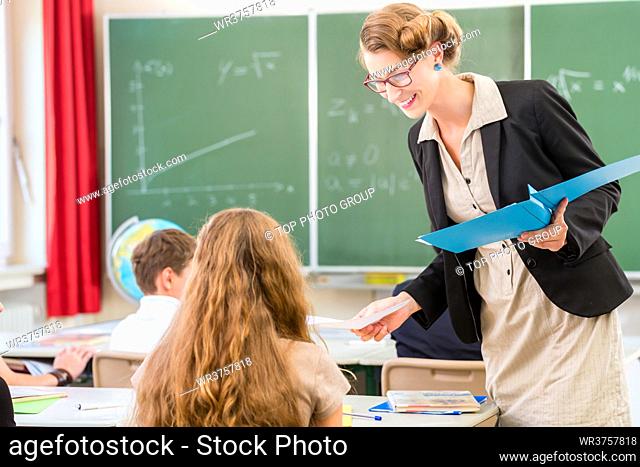 Teacher or docent or educator giving while lesson in front of a blackboard or board a sheet of paper and educate or teaching students or pupils or mates in a...