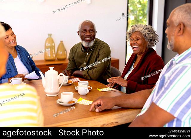 Multiracial cheerful senior friends with bingo, coffee and cookies on dining table in nursing home