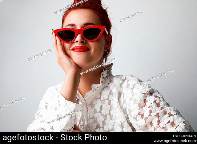 Beautiful woman in lace white dress wearing red sunglasses posing on gray background. High quality photo