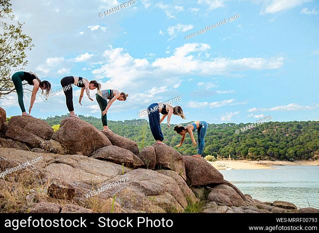 Young women with instructor practicing yoga on rock