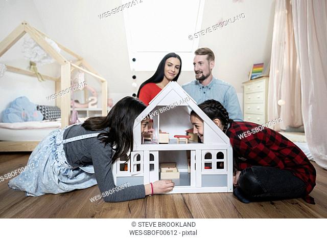 Parents and twin daughters playing with doll house in nursery